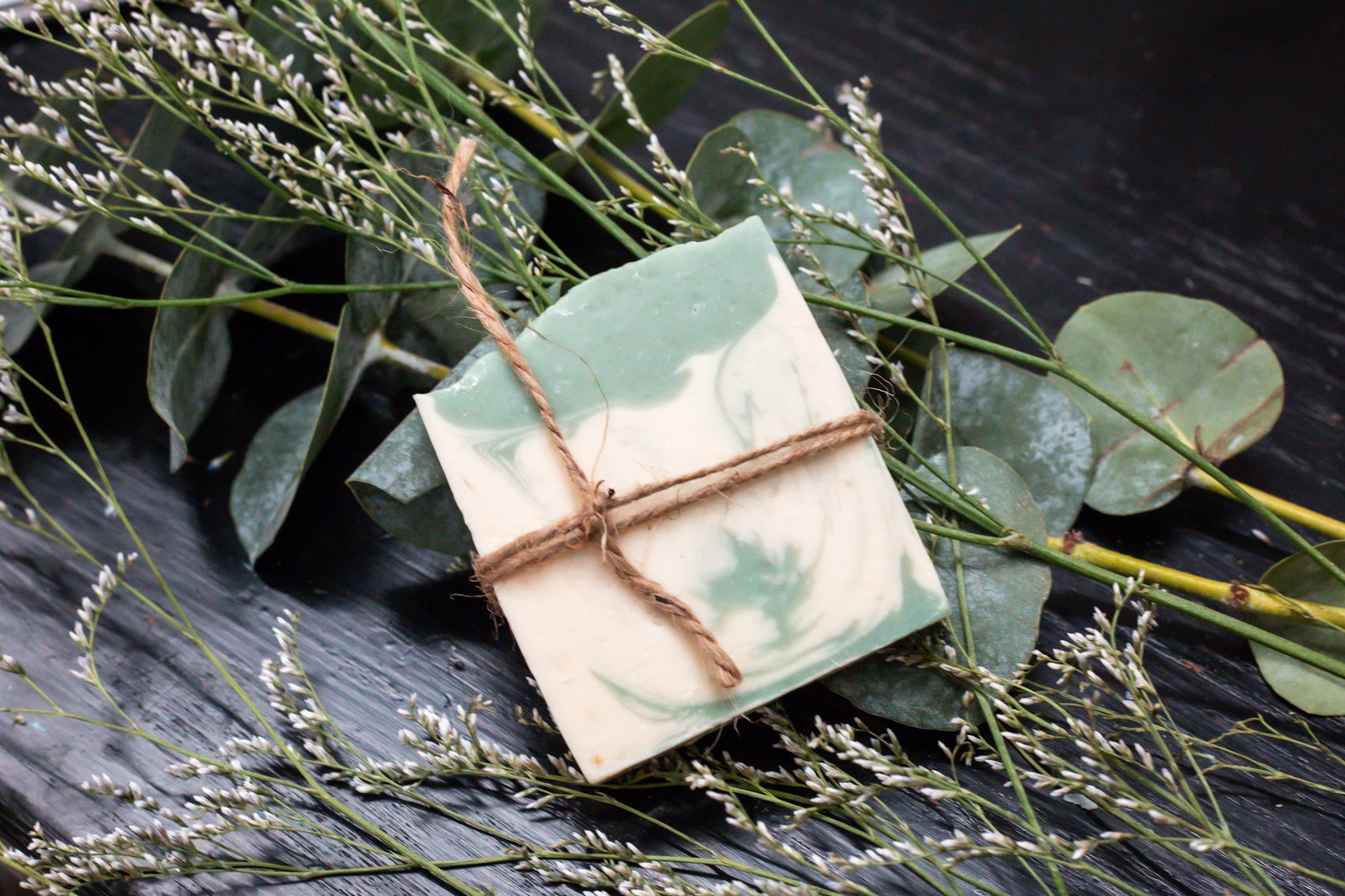 Bar of soap tied with twine on a dark surface with greenery