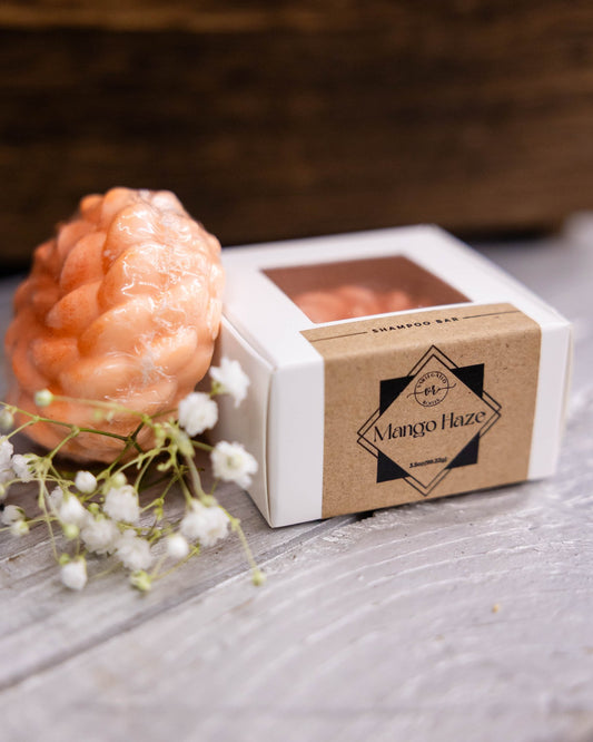 Coral-colored soap bar in a box labeled 'Mango Haze' on a wooden surface with flowers